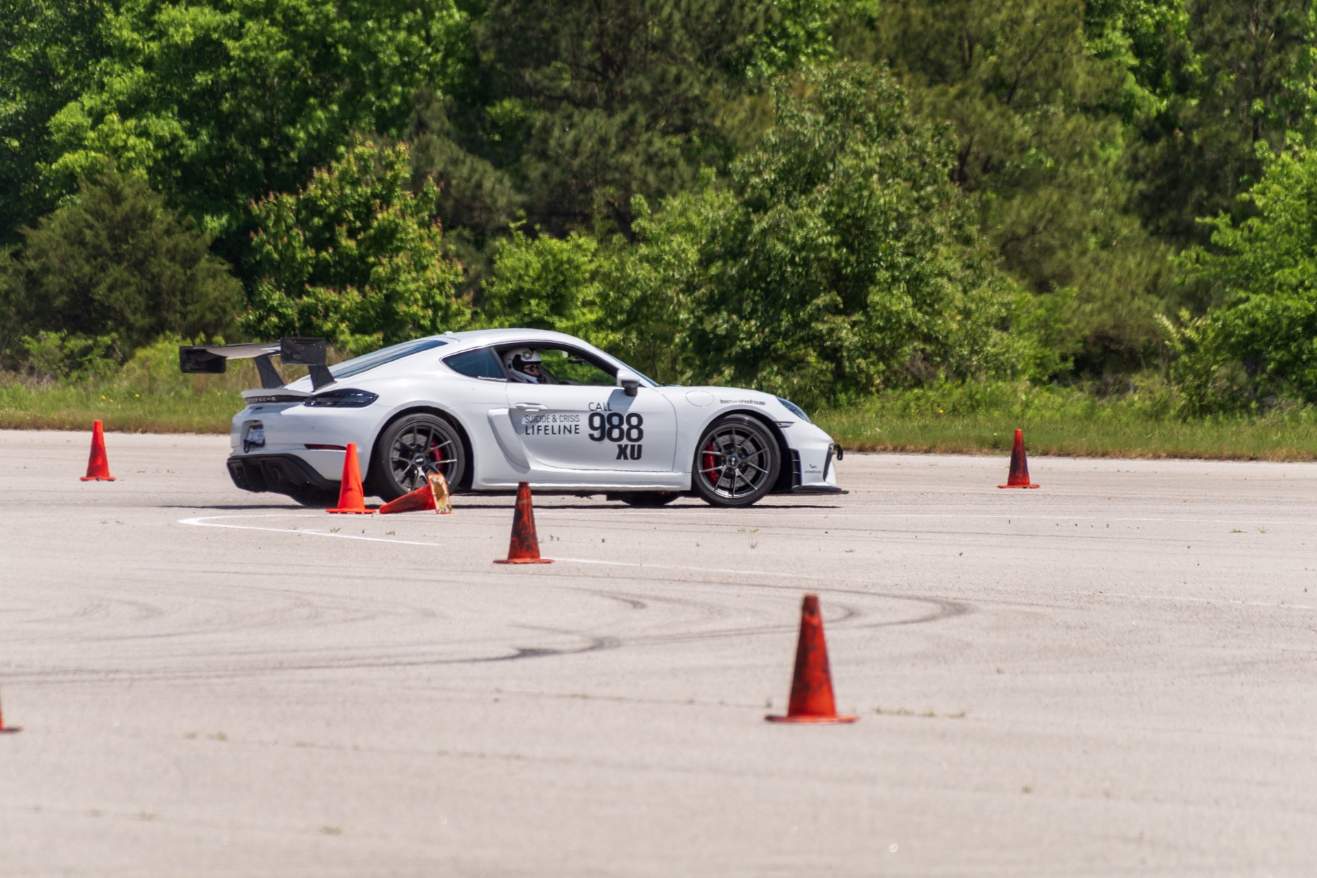 Side profile of Team Wheelhouse Porsche Cayman GT4 988 mid-corner under Carolina clouds
