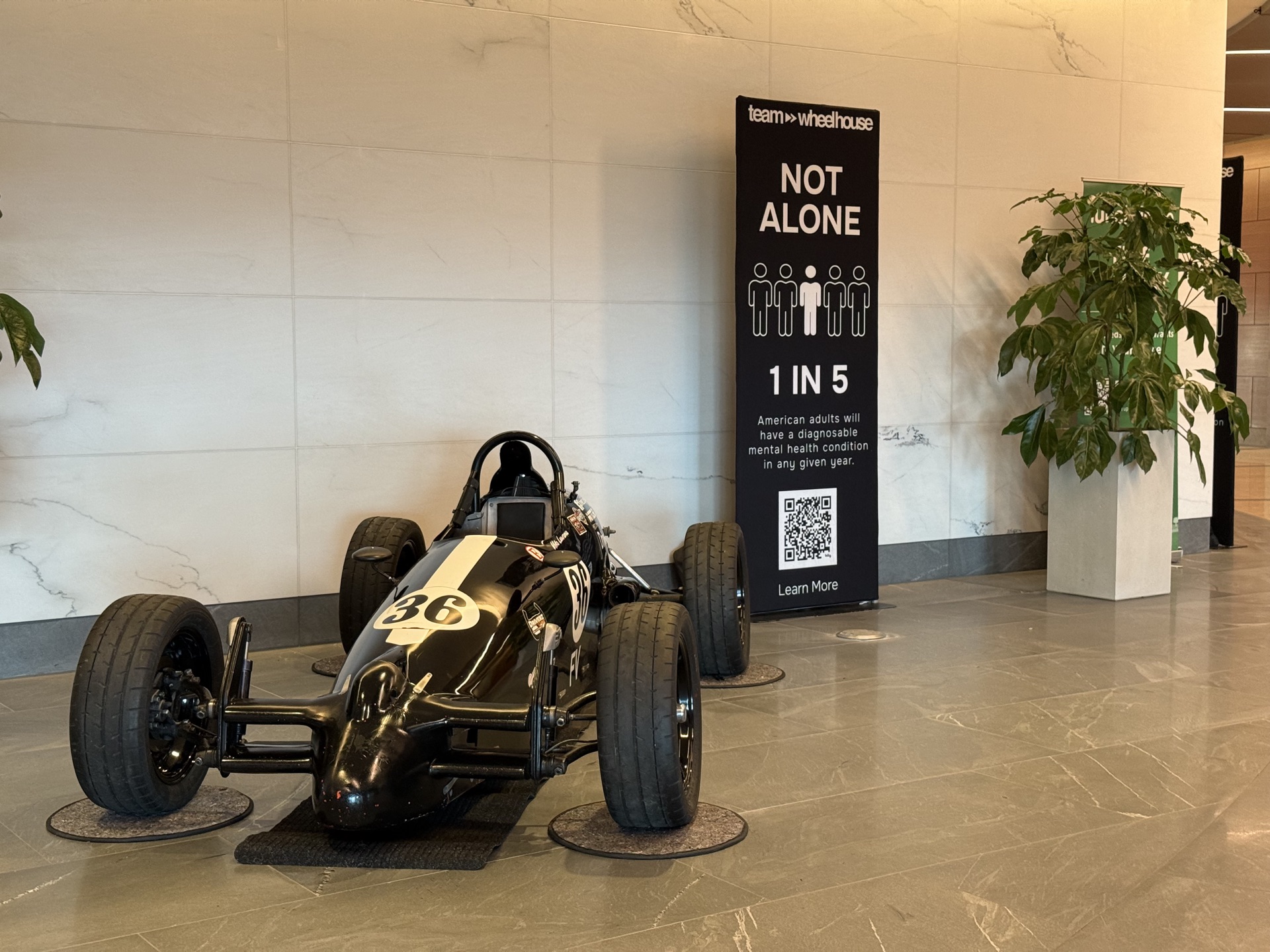 Vintage formula race car beside a Team Wheelhouse 1-in-5 mental health banner in Legacy Union lobby