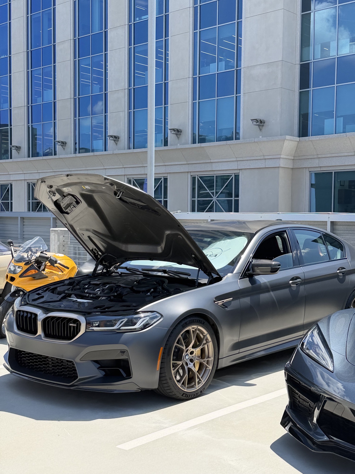 Black BMW M-series with hood up parked beside the Charlotte glass-tower backdrop