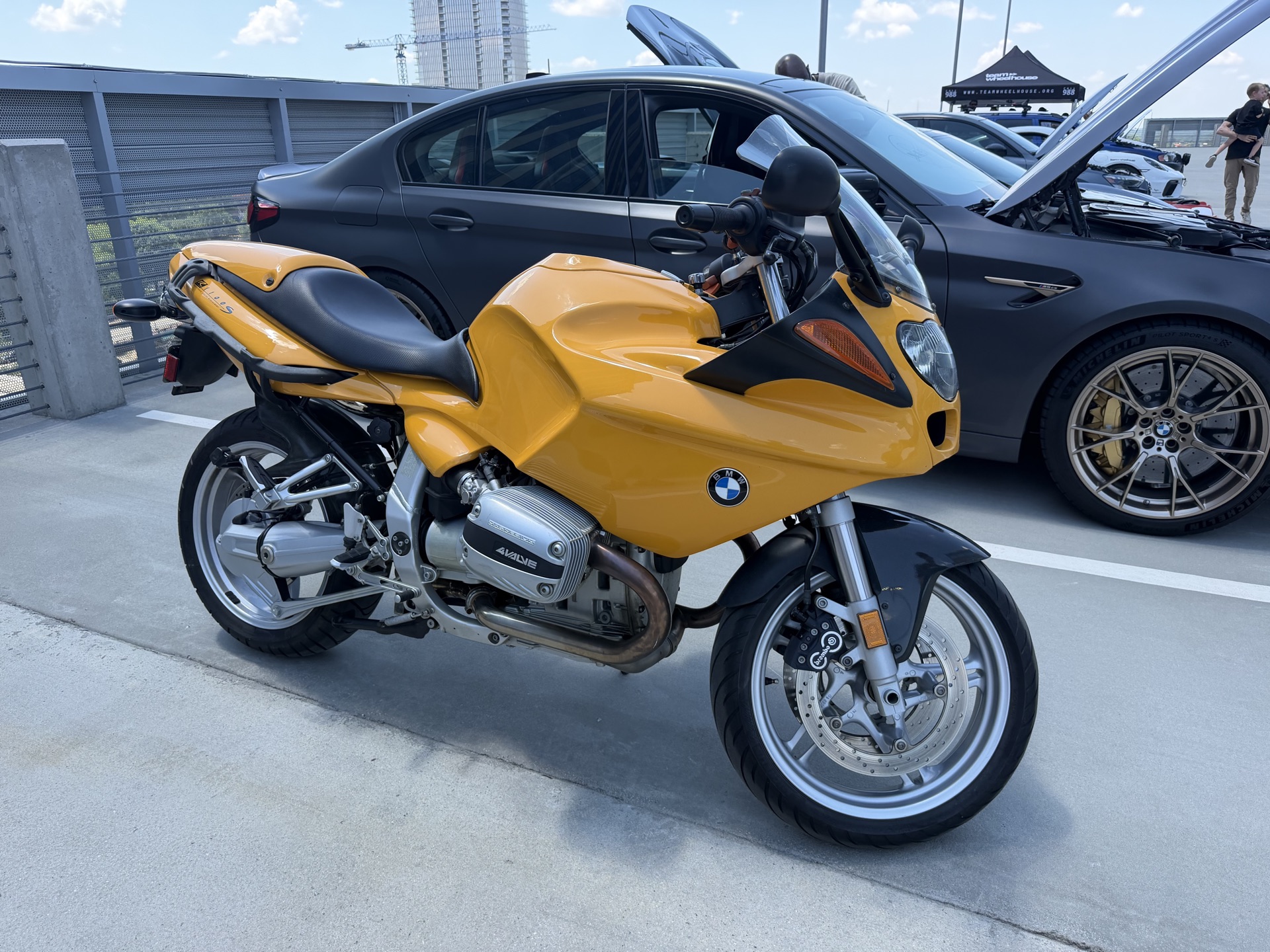 Yellow BMW R 1100 S motorcycle in front of a black BMW sedan on the rooftop deck