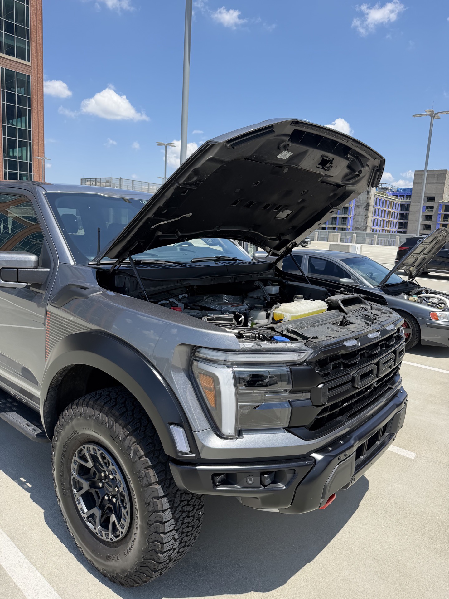 Tan Ford Bronco Raptor with hood raised against the Charlotte skyline