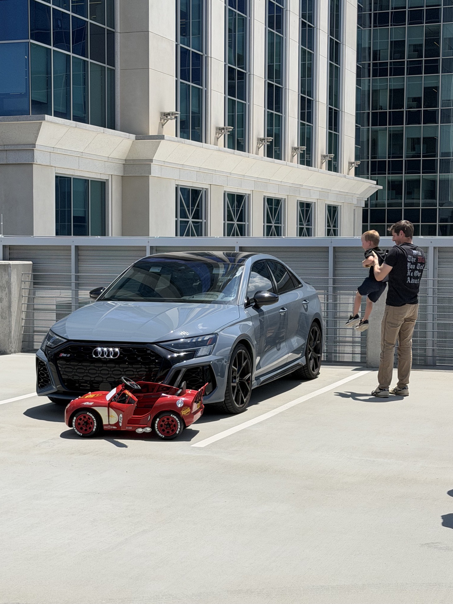 Attendees admire a slate-grey Porsche Cayman GT4 next to a Lightning McQueen ride-on car