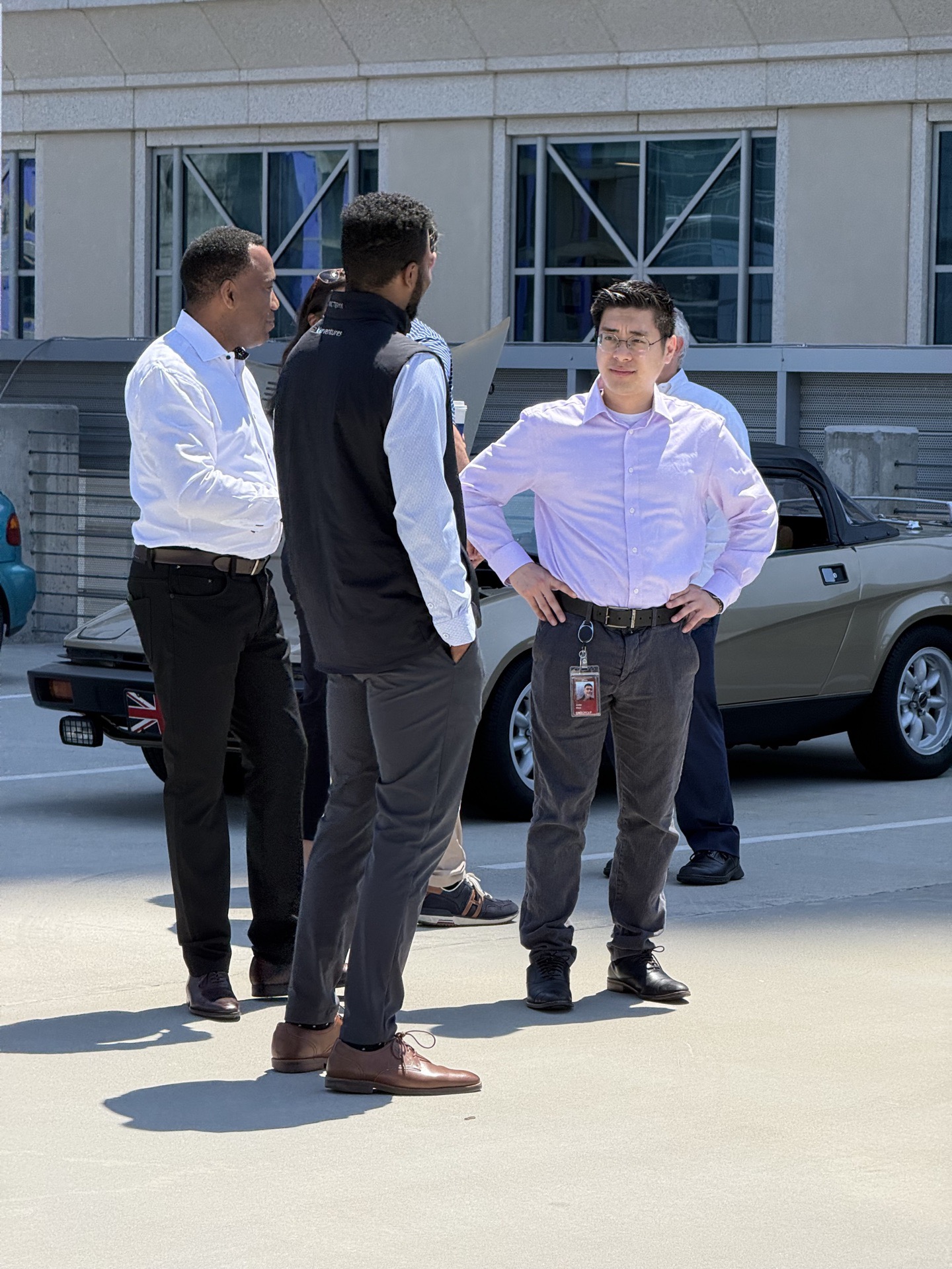 Three attendees in dress shirts in front of a brown Triumph TR7 wedge at the rooftop meet